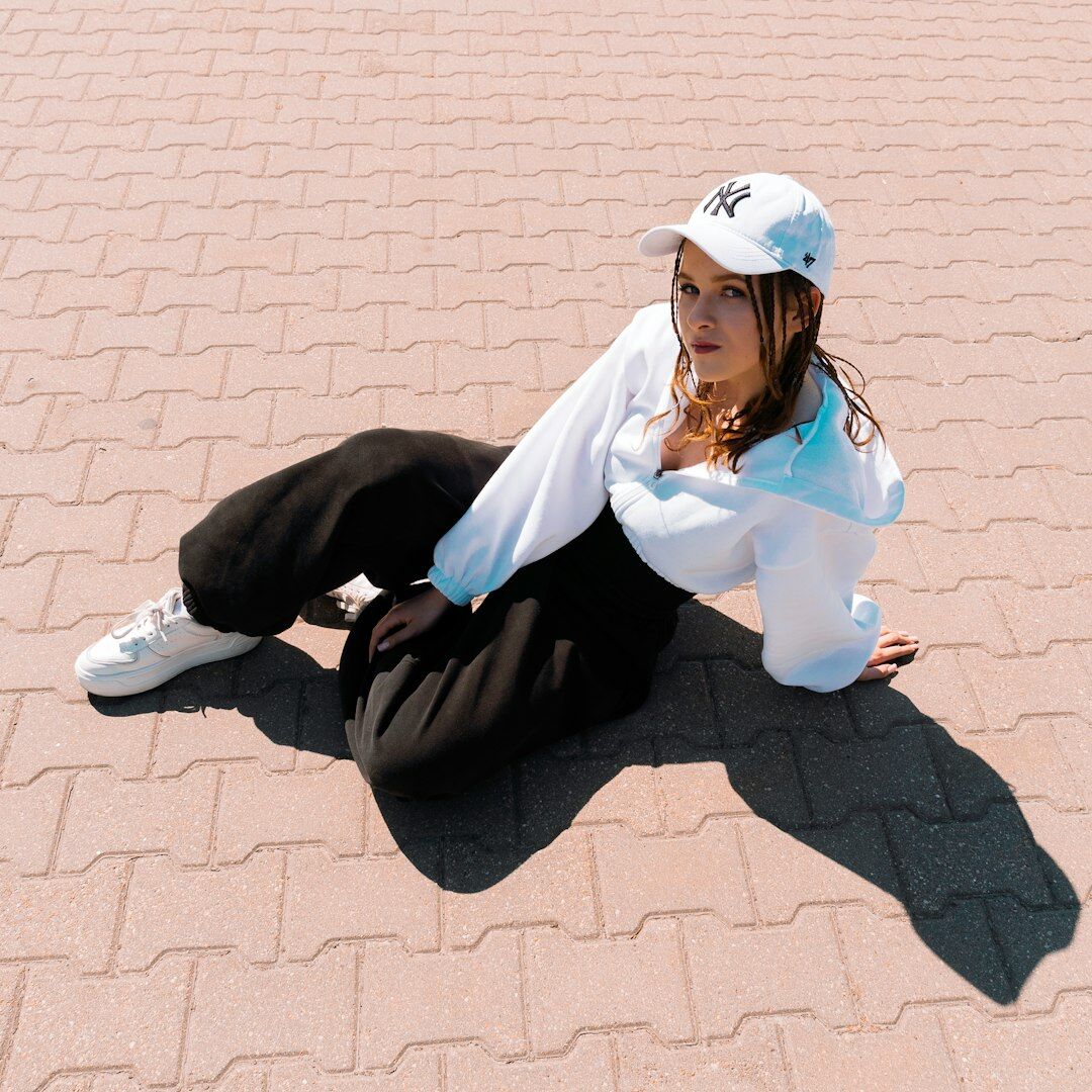 Young woman in white cap and top sitting on pavement