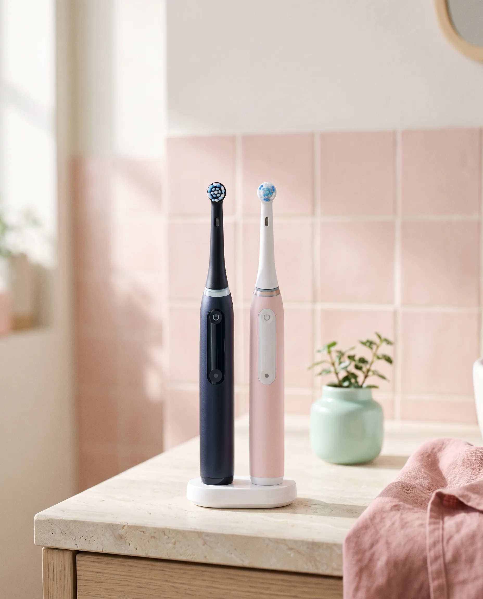 Twee elektrische tandenborstels, zwart en roze, op één oplaadstation in een lichte badkamer